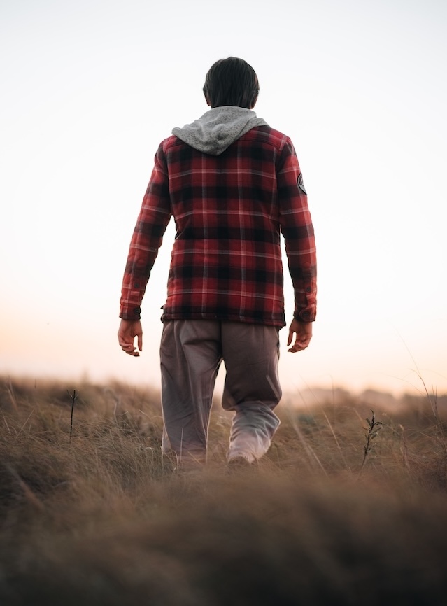 A vertical shot of a young man walking in the forest at sunset