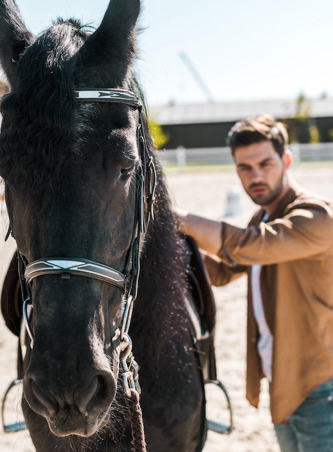 selective focus of male equestrian fixing horse saddle at ranch