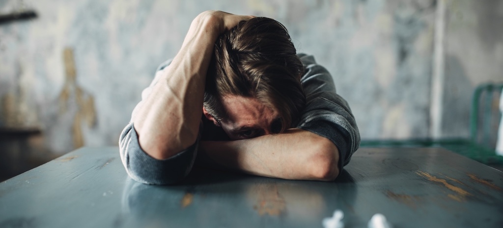 Male sitting at the table with drugs and syringe, grunge room interior on background.