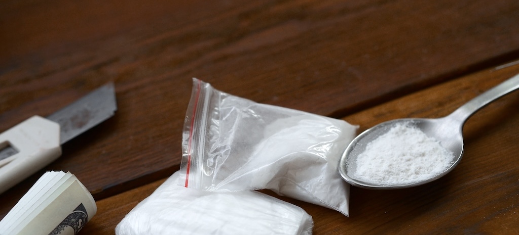 Lighter paper knife and spoon full of white powder on wooden background.