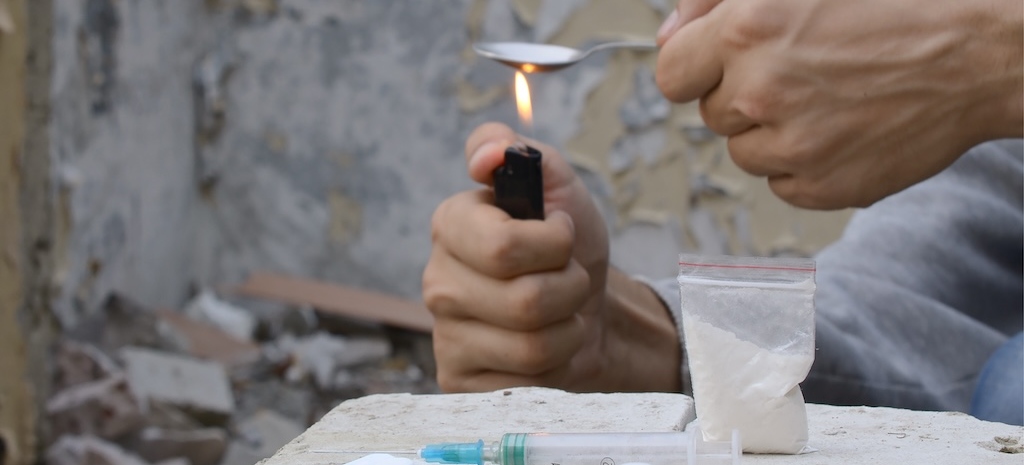 Hands of drug user melting cocaine in a spoon holds over a cigarette lighter. 